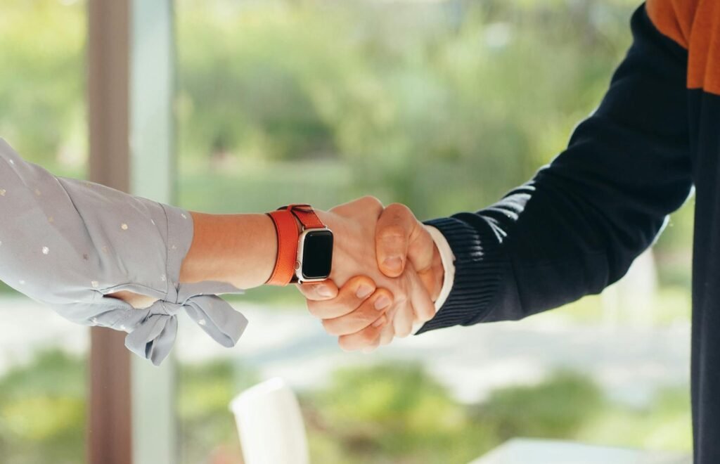 Close-up of a handshake between two adults, one wearing a smartwatch, set in an outdoor environment.